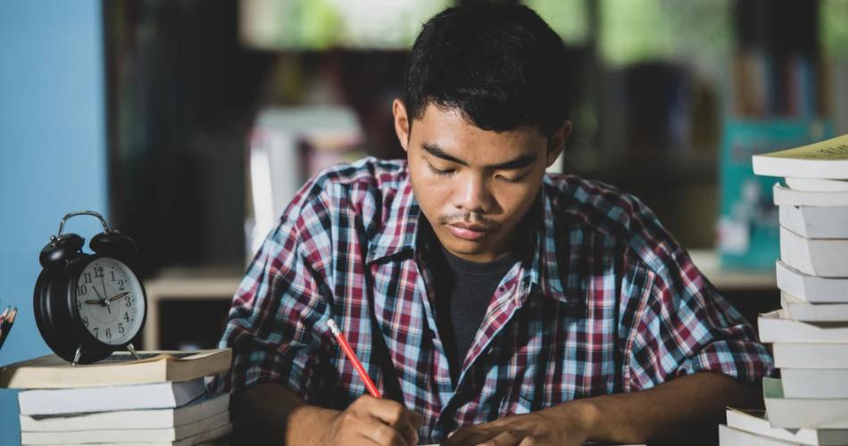 Student studying for CUET UG 2025 Accountancy exam with books and clock on desk, representing NTA revised exam structure