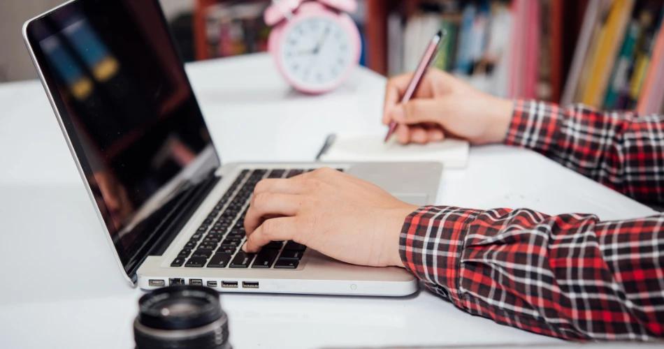Student using a laptop and writing, likely preparing to challenge the NEET UG 2025 provisional answer key online