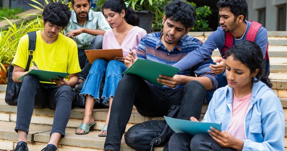 Students gathered on stairs, studying and working on assignments, with a banner showcasing the Maharashtra FYJC 2025 General Merit List Release